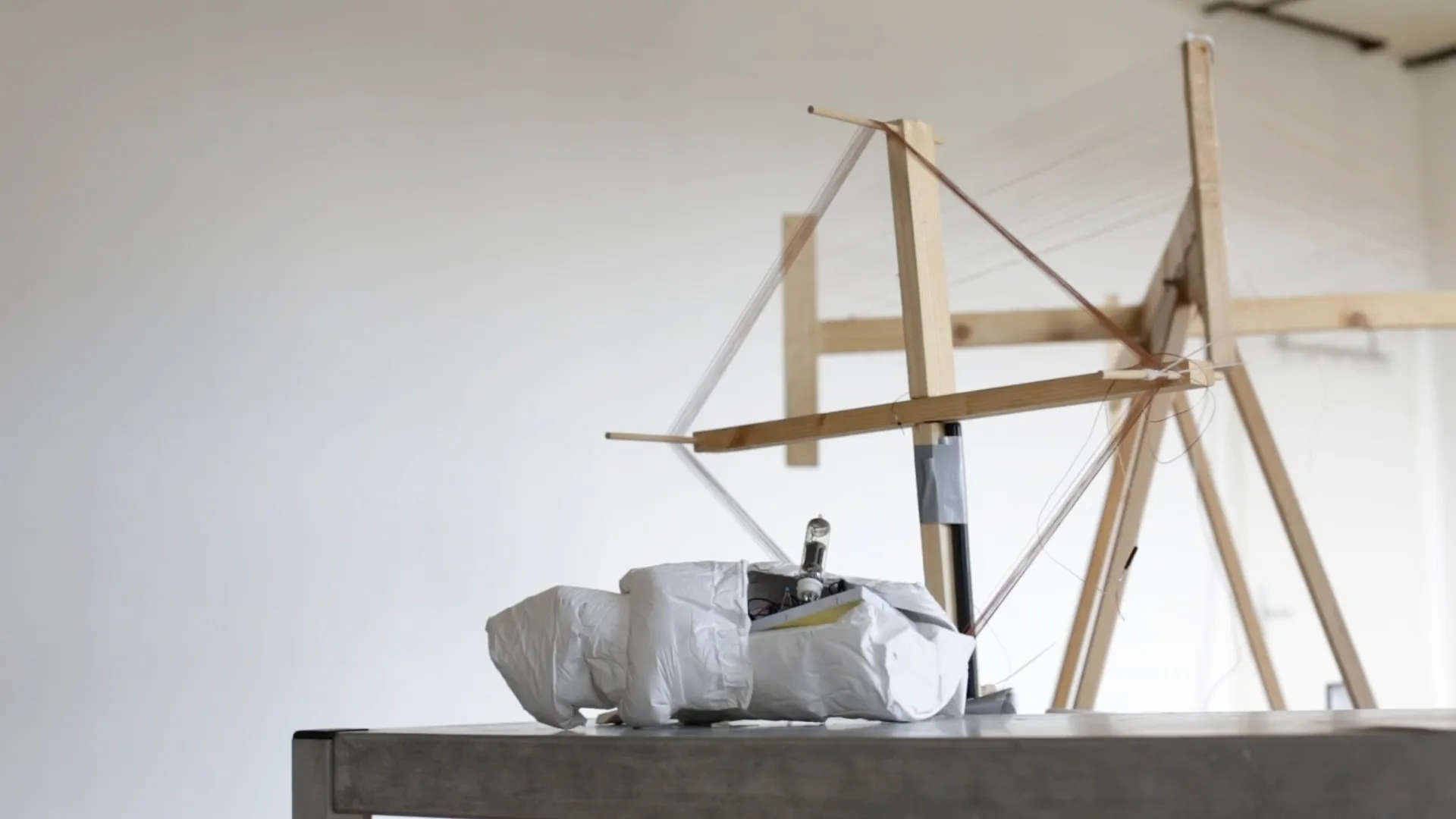 A wooden frame with taut threads on a tripod in a bright studio room
